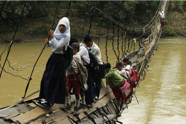 Students hold on to side steel bars of a collapsed bridge as they cross a river to get to school at Sanghiang Tanjung village in Lebak regency