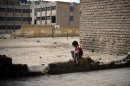 A boy sits next to a heavily damaged school in the northern Syrian city of Aleppo on April 17, 2013
