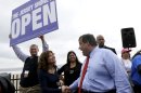 New Jersey Gov. Chris Christie, right, talks to Carla Pilla, of Seaside Heights, N.J., while Robert Hilton, left, executive director of the Jersey Shore Convention and Visitor's Bureau, holds a sign, Friday, May 24, 2013, in Seaside Heights, N.J. Christie cut a ribbon to symbolically reopen the state's shore for the summer season, seven months after being devastated by Superstorm Sandy. Several beach communities have annual beach ribbon cuttings, announcing they are back in business. But this year's ceremonies are more poignant seven months after a storm that did an estimated $37 billion of damage in the state. (AP Photo/Julio Cortez)