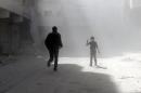 A Syrian young boy flashes the sign of victory amid dust as a man runs in a street of the northern city of Aleppo following a reported Syrian government forces air strike on February 21, 2014