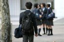 High school student walks towards a group of female students chatting in front of a school in Tokyo