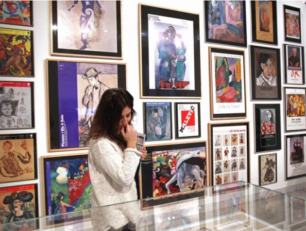 Una visitante junto a un grupo de carteles expuestos en el Museo Picasso que plantea en una muestra un viaje por las 79 exposiciones temporales que han difundido la obra del pintor malagueño en los 50