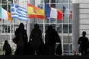 Pedestrians walk towards the Irish, Greek, Spanish and French national flags outside the European Parliament in Brussels