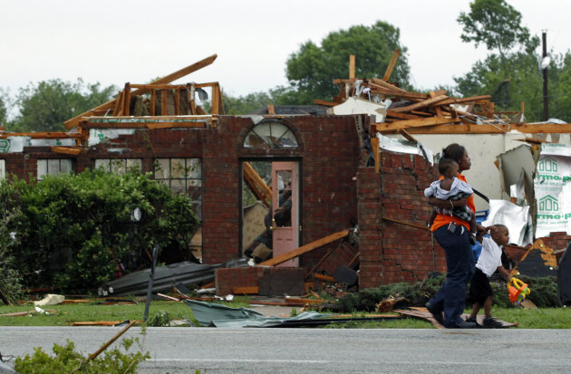 A woman and two children walk past a damaged house after a tornado struck a residential neighborhood in Lancaster