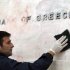 A worker cleans the sign of the Bank of Greece from red and black paint, after Sunday's riots, in Athens, on Tuesday, Feb. 14, 2012. Firefighters doused smoldering buildings and cleanup crews swept rubble from the streets of central Athens following a night of rioting during which lawmakers approved harsh new austerity measures demanded by bailout creditors to save the nation from bankruptcy.  (AP Photo/Thanassis Stavrakis)