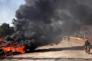 Rebel fighters drive past burning tyres, set ablaze to shield them from warplanes above, on November 3, 2016, at an entrance to Aleppo during a rebel offensive to break a three-month siege of the opposition-held east of the city