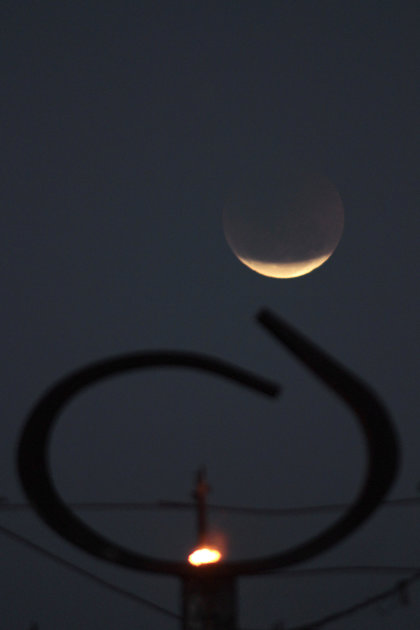 The earth casts its shadow over the moon during a total lunar eclipse seen from behind the Pantheon of Freedom sculpture, featuring a torch, at Three Powers Square in downtown Brasilia, Brazil, Wednes