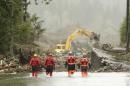 Four search and rescue workers wade through water covering Washington Highway 530 Thursday, March 27, 2014, on the eastern edge of the massive mudslide that struck Saturday near Darrington, Wash. as heavy equipment moves trees and other debris in the background. (AP Photo/Ted S. Warren, Pool)