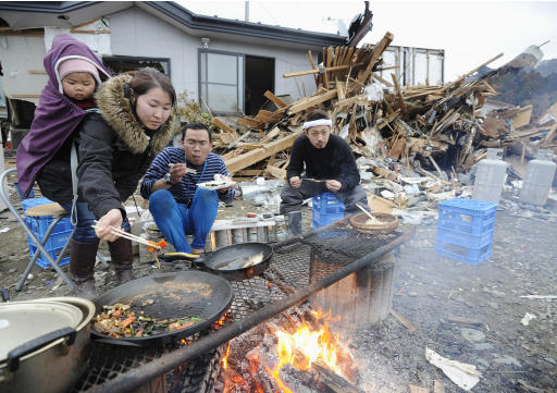 Sobrevivientes de un maremoto, que devastó gran parte del litoral nororiental del Japón, cocinan y comen al aire libre frente a su vivienda destruida el martes 15 de marzo del 2011 en el pueblo de Ishinomaki, de la prefectura de Miyagi, cuatro días después del desastre que siguió a un catastrófico terremoto. (Foto AP/Kyodo News)