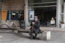 An elderly man sits in front of a closed branch of Bank of Cyprus as a youth makes a transaction at an ATM in Nicosia