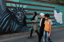 An Iranian family walks past anti-US graffiti on the wall of the former US embassy in Tehran, on July 14, 2015