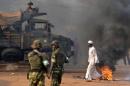 A man walks past burning tyres as French troops of the Sangaris Operation (back) and Burundian soldiers from the African-led International Support Mission to the Central African Republic (MISCA) deploy in Bangui on January 2, 2014