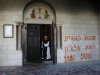 A monk stands next to graffiti sprayed on a wall at Monastery near Jerusalem
