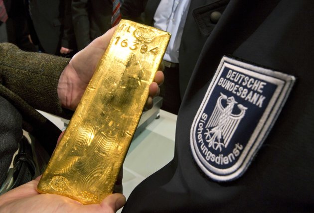 A journalist holds a gold ingot next to a security officer of the German Central Bank, right, in Frankfurt, Germany, Wednesday Jan. 16, 2013. Germany's central bank is to bring back home some US $36 billion ( 27 billion euro) worth of gold stored in the United States and France.The Bundesbank said in a statement Wednesday that it will repatriate all 374 tons of gold it had stored in Paris by 2020. An additional 300 tons - equivalent to 8 percent of the Bundesbank's total reserves worth about $183 billion _ will also be shipped from New York to Frankfurt. Frankfurt will hold half of Germany's 3,400 tons of gold by 2020, with New York retaining 37 percent and London storing 13 percent. The move follows criticism from Germany's independent Federal Auditors' Office last year bemoaning the central bank's oversight of gold reserves abroad. (AP Photo/dpa/ Frank Rumpenhorst)