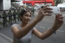 A woman stops to take a selfie with Thai soldiers stand guard near Victory Monument in Bangkok, Thailand, Friday, May 30, 2014. An anti-coup activist called Friday for a weekend rally to defy the military government's ban on demonstrations, urging those opposed to the takeover to wear masks and be ready for cat-and-mouse chases with soldiers in the capital. (AP Photo/Sakchai Lalit)