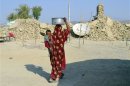 A survivor of an earthquake carries a pot on her head filled with drinking water as she walks near the rubble of a mud house after it collapsed following the quake at Dhallbedi Peernder village in Awaran district