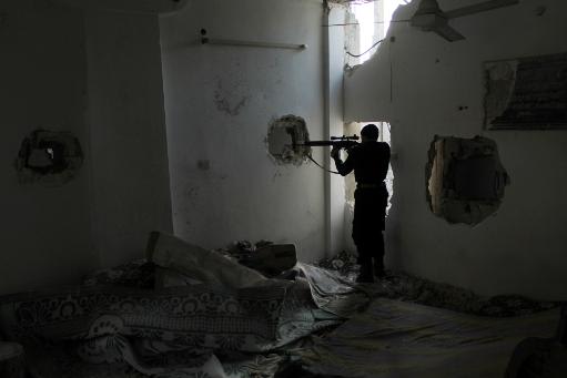 A rebel fighter points his weapon through a hole in the wall of a damaged building in the northeastern city of Deir Ezzor during fighting with Syrian government forces on December 1, 2013