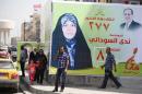 Iraqis walks past a large banner showing election candidate Nada al-Sudani running on the electoral list of Iraqi Prime Minister Nuri al-Maliki (top right) placed along a street in the capital Baghdad, on April 1, 2014