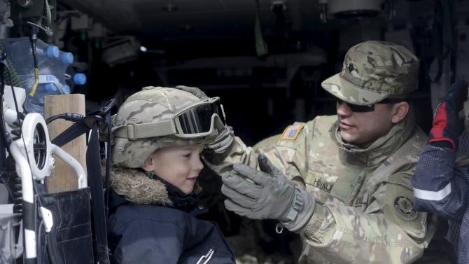 A soldier of the U.S. Army 2nd Cavalry Regiment deployed in Estonia adjusts a helmet on the boy&#39;s head during the stop at the &quot;Dragoon Ride&quot; exercise in Riga