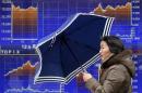 A pedestrian holding an umbrella walks past an electronic board displaying graphs of the recenent movement of Japan's Nikkei average outside a brokerage in Tokyo