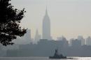 The haze shrouded skyline of New York is a backdrop for a boat moving up the Hudson River in Hoboken