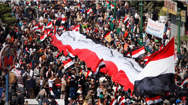 Egyptians carry a large national flag with Arabic writing that reads, "President before constitution," in Tahrir Square during the first anniversary to mark the beginning of the popular uprising that 