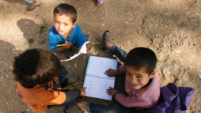 Boys play with a school book at a UNHCR camp for Syrian refugees in south Lebanon on April 14, 2015