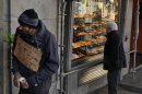 A man begs money with a banner reading "I have three kids, help me please, thank you, happy christmas, god bless you" as a woman looks at 'Three Kings' cakes outside a bakery shop in Madrid, Sunday, Jan. 6, 2013. (AP Photo/Andres Kudacki)