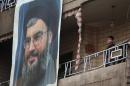 A Lebanese boy stands on his balcony next of a large portrait of Hezbollah leader Sheik Hassan Nasrallah at the site of a car bombing in a southern suburb of Beirut, Lebanon, Wednesday, Jan. 22, 2014. An explosion ripped through a Shiite neighborhood in south Beirut on Tuesday targeting supporters of Lebanon's militant Shiite Hezbollah group. Hezbollah has sent its gunmen to fight alongside Assad's forces, providing a significant boost to the Syrian government's overstretched military. Hezbollah's critics say the group's armed intervention in Syria has stoked sectarian tensions at home and needlessly dragged Lebanon into the maelstrom next door. (AP Photo/Hussein Malla)