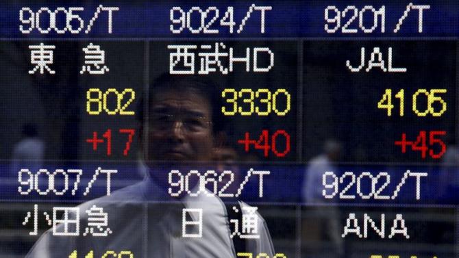 A pedestrian is reflected in an electronic board showing the various stock prices outside a brokerage in Tokyo