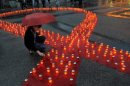A woman lights a candle on a symbolic red ribbon in remembrance of individuals who have died of AIDS