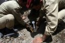 Yemeni security forces disarm an unexploded mortar shell that landed in the ground during clashes
