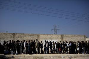 Men wait to be searched by the Syrian military after …