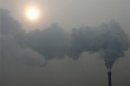 A chimney billows smoke as the sun shines through haze on a cold winter's day in Beijing