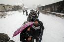 Migrants wait in line to receive free food during a snowfall outside a derelict customs warehouse in Belgrade