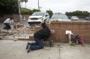 Akiva Sherman, right, 62, repairs the wall next to a makeshift memorial Sunday, June 9, 2013, where a victim's vehicle crashed during the shootings at Santa Monica College in Santa Monica, Calif. The shootings on Friday left six people dead, including the gunman. (AP Photo/Ringo H.W. Chiu)