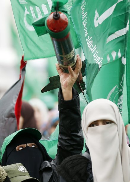 A Palestinian woman holds a model of the Qassam rocket during a rally marking the 25th anniversary of the founding of Hamas, in Gaza City
