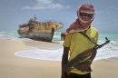 In this photo taken Sunday, Sept. 23, 2012, masked Somali pirate Hassan stands near a Taiwanese fishing vessel that washed up on shore after the pirates were paid a ransom and released the crew, in the once-bustling pirate den of Hobyo, Somalia. The empty whisky bottles and overturned, sand-filled skiffs that litter this shoreline are signs that the heyday of Somali piracy may be over - most of the prostitutes are gone, the luxury cars repossessed, and pirates talk more about catching lobsters than seizing cargo ships. (AP Photo/Farah Abdi Warsameh)