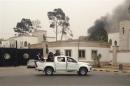 Armed men aim their weapons from a vehicle as smoke rises in the background near the General National Congress in Tripoli