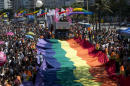 A man poses stands on a giant gay movement flag during the Gay Pride Parade at Copacabana beach in Rio de Janeiro, Brazil, Sunday, Nov.16, 2014. Thousands took part in Rio de Janeiro's 19th Gay Pride parade, to fight for a more just and inclusive society, which recognizes equal rights for all the gay community. (AP Photo/Silvia Izquierdo)