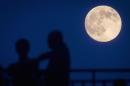 People stand and look at the moon one day ahead of the Supermoon phenomenon from a bridge over 42nd St. in the Manhattan borough of New York