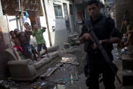 In this photo taken April 11, 2012, police from the Special Operations Battalion (BOPE) patrol as children joke in the Manguinhos slum in Rio de Janeiro, Brazil. Setbacks in a security program meant to take back territory from the drug trade have shown the immense challenge of pacifying the city’s violent slums and raised questions about the state's ability to keep the peace as Rio prepares to take the world stage not just for the Olympics but the 2014 World Cup, which will host its headline events in Rio. (AP Photo/Felipe Dana)