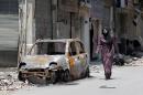 A Syrian woman walks past a burnt car on May 12, 2014 in a destroyed neighbourhood of the Old City of Homs