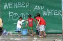Bambini trasportano secchi d'acqua potabile davanti ad un graffito con la richiesta di aqua e cibo a Tecloban, città delle Filippine centrali devastata da un potentissimo tifone che ha ucciso almeno 10.000 persone