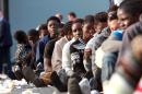 Migrants sit in line after disembarking from a ship in the port of Catania on the coast of Sicily on June 8, 2015
