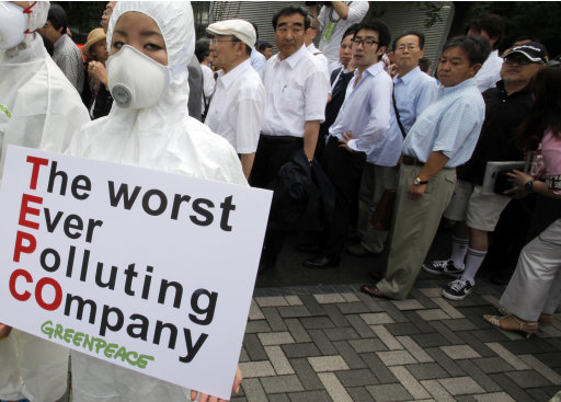 A Greenpeace protester in protective gear holds a banner as shareholders, rear, arrive for the annual shareholders' meeting of Tokyo Electric Power Co. in Tokyo on Tuesday June 28, 2011. Executives at the Japanese utility behind the nuclear power plant sent into meltdown by the March quake apologized to investors who repeatedly interrupted the shareholders' meeting with heckles, yells and questions of outrage. (AP Photo/Itsuo Inouye)