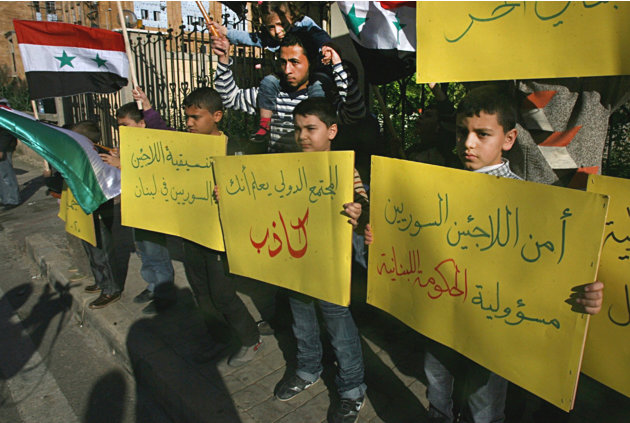 Niños y otros refugiados sirios que huyeron a Líbano por la violencia en su país sostienen pancartas que leen en árabe "La seguridad de los refugiados sirios es responsabilidad del gobierno libanés" (