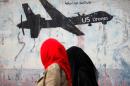 Women walk past a graffiti, denouncing strikes by U.S. drones in Yemen, painted on a wall in Sanaa, Yemen