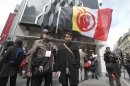 A French supporter of the Indian cause, who refused to give his name, left, holds a flag of the American Indian Movement and an American exchange student, member of the Arizona's Hopi tribe, Bo Lomahquahu, right, stand outside of the Druout's auction house to protest the auction of Native American Hopi tribe masks in Paris, Friday, April 12, 2013. A contested auction of dozens of Native American tribal masks went ahead Friday afternoon following a Paris court ruling, in spite of appeals for a delay by the Hopi tribe, its supporters including actor Robert Redford, and the U.S. government. (AP Photo/Michel Euler)