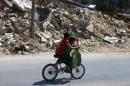 Boys ride a bicycle near rubble of damaged buildings, in the rebel held besieged town of Douma